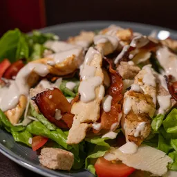 Insalata Caesar con pollo grigliato a fette, bacon croccante, lattuga, pomodori, crostini e salsa cremosa