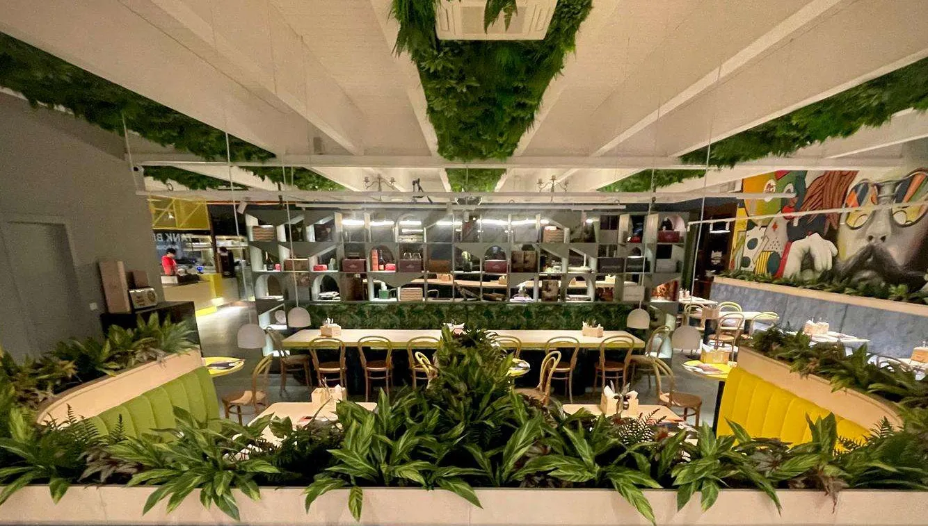 Vista interna del locale con tavoli, sedute colorate e numerose piante decorative che creano un ambiente accogliente